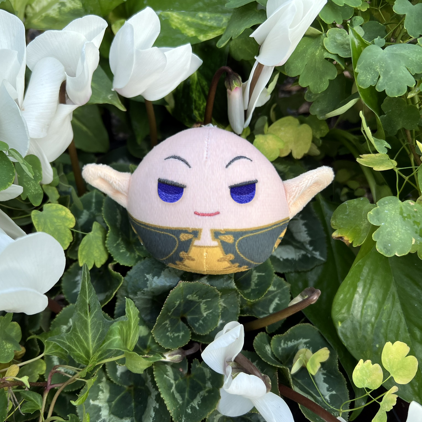 A photo from above of the Solas Keychain Plush resting in a thick bundle of green clover and white flowers.