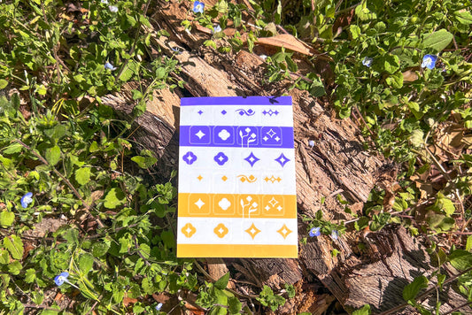 A single sheet of Speedwell Tab Divider Stickers photographed against the vibrant green and indigo of living Speedwell flowers.