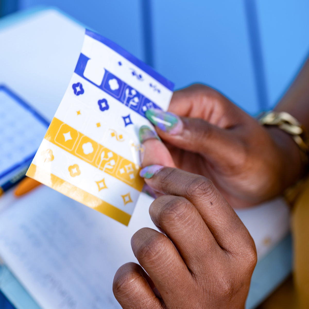 A close-up of a person's hands peeling a Tab Divider Sticker off its backer to place inside their notebook. The calendar sticky note can be seen inside the notebook.