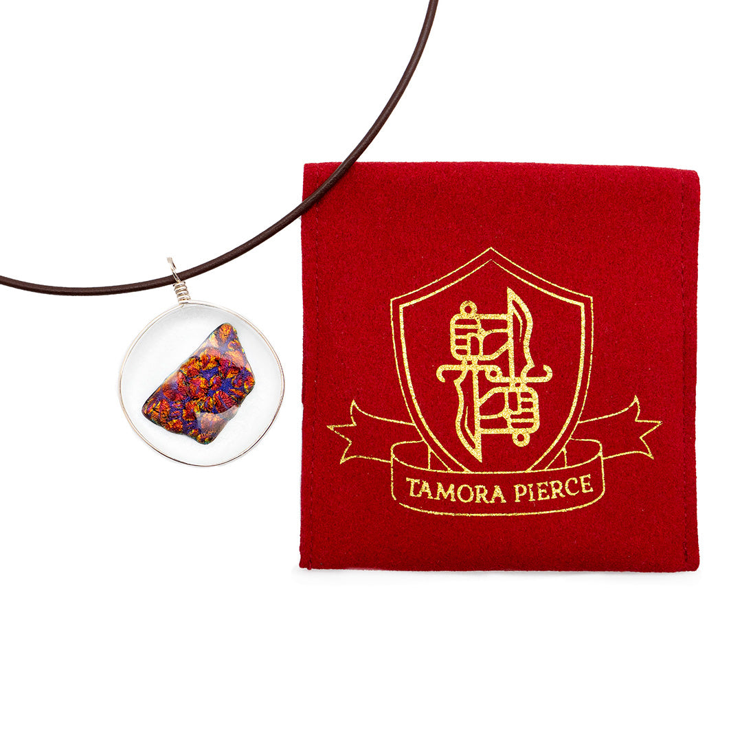 on the left is the ember glass pendant. on the right is a red jewelry pouch with a gold DWS and Tamora Pierce logo.