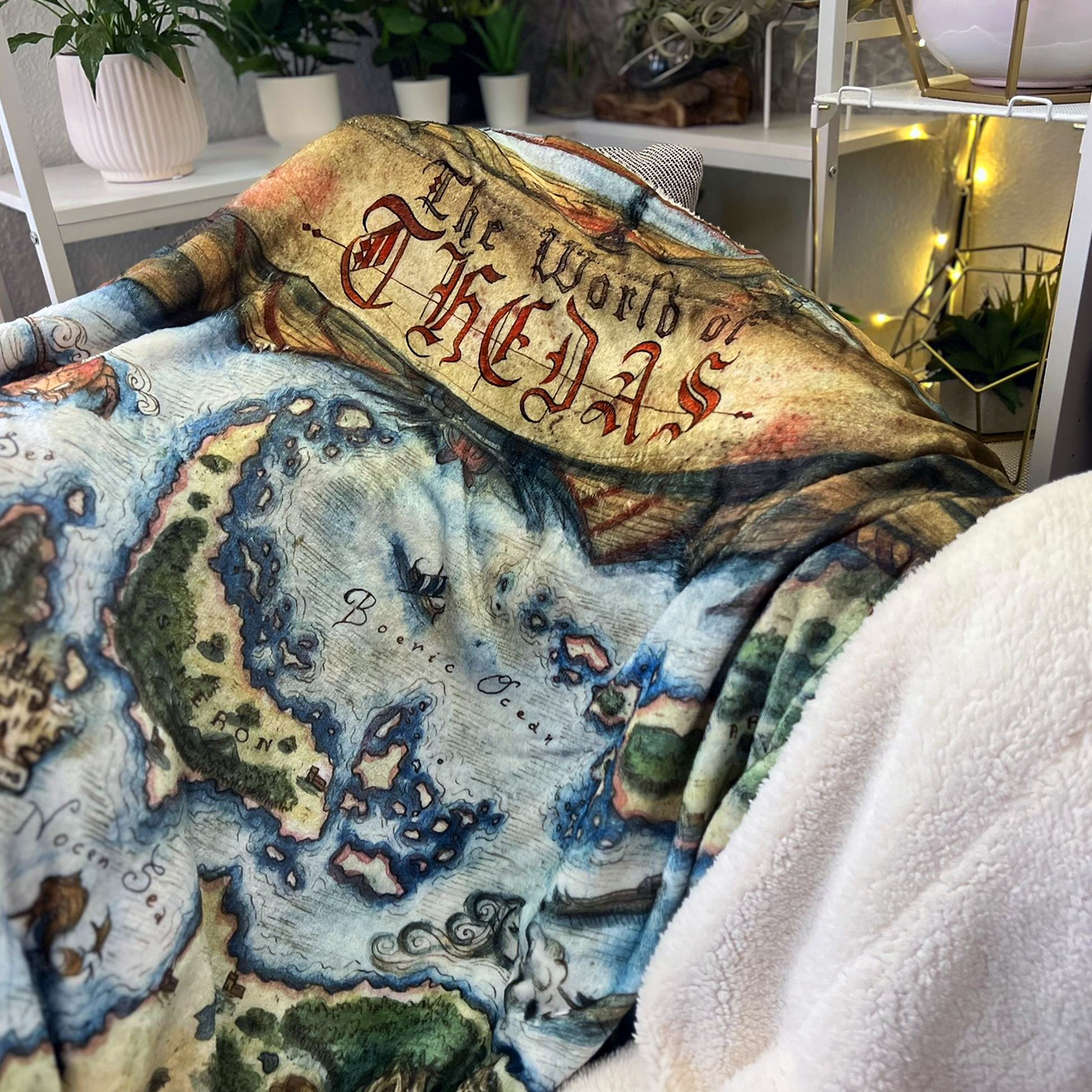 A closeup of the Thedas Map Blanket, focused on the Boeric Ocean, and the banner at the top of the blanket that reads "The World of Thedas." The blanket is draped over a chair.