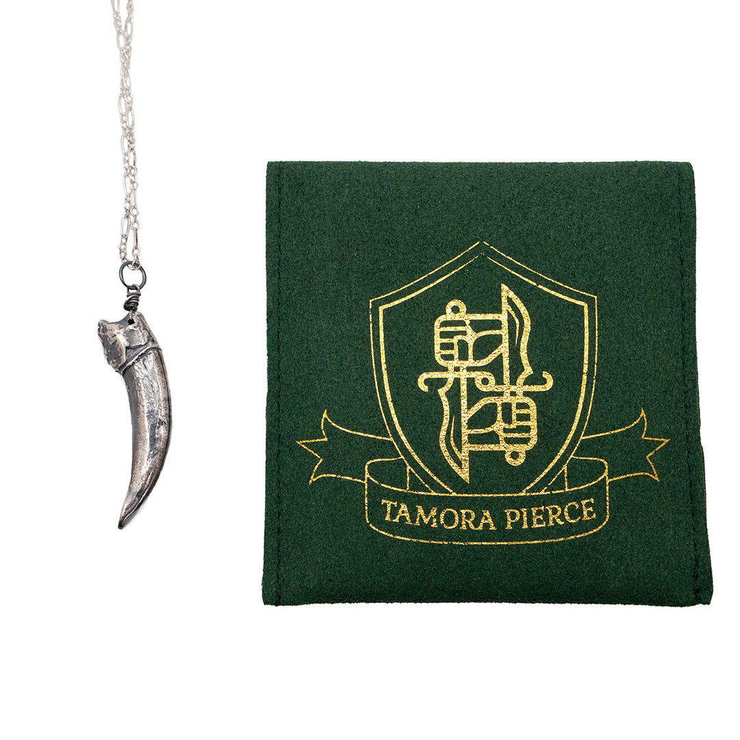 on the left is a close-up of the silver badger claw pendant. on the right is the front of the green jewelry pouch, which has a DWS and Tamora Pierce logo in gold.