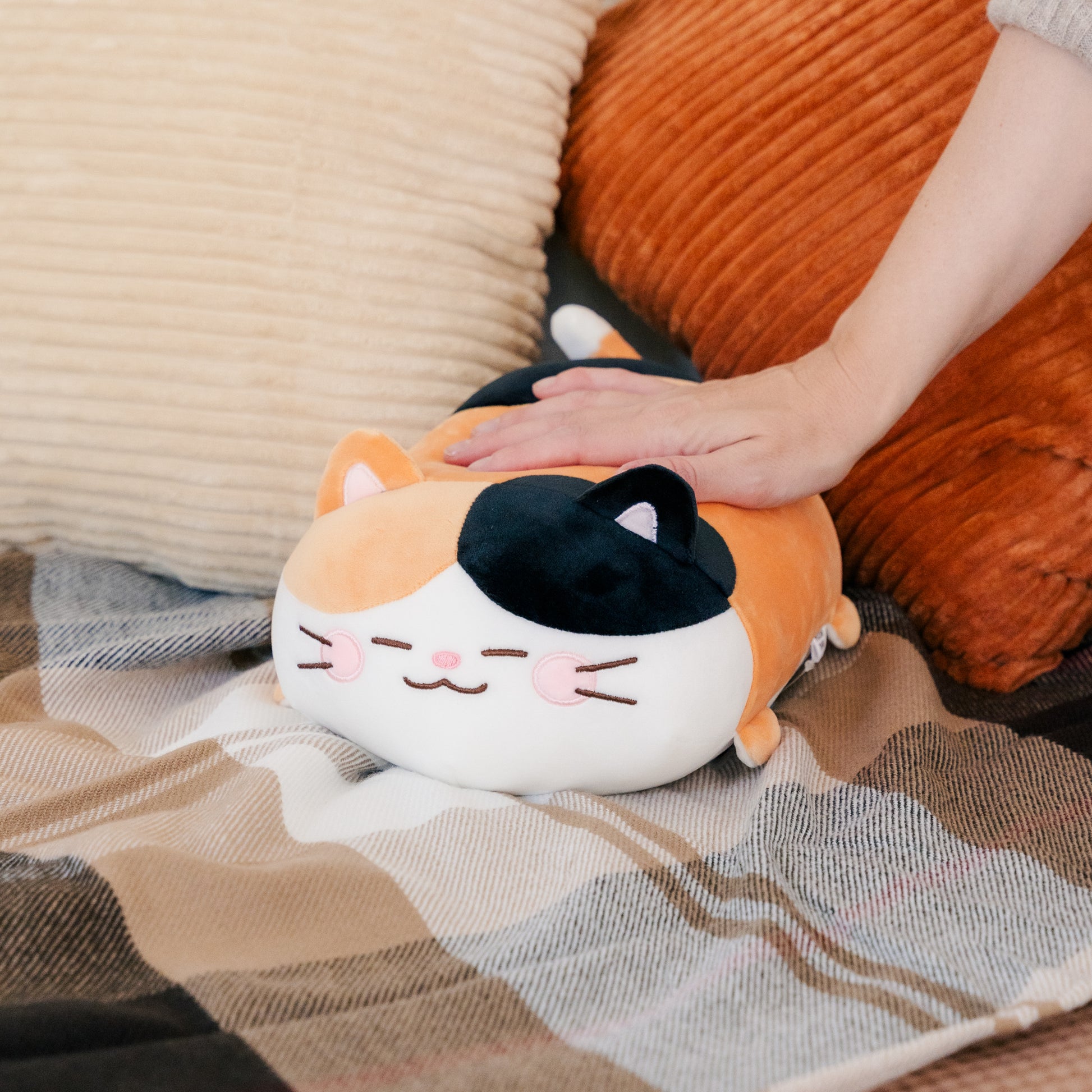 Camang plush resting on a blanket with a model's hand on its back.