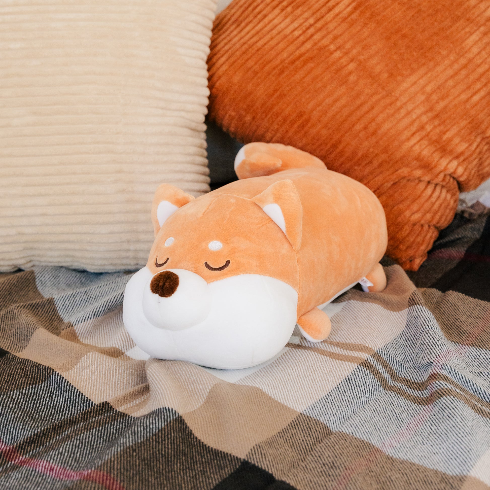 The Shiba cushion resting on a blanket and pillows.