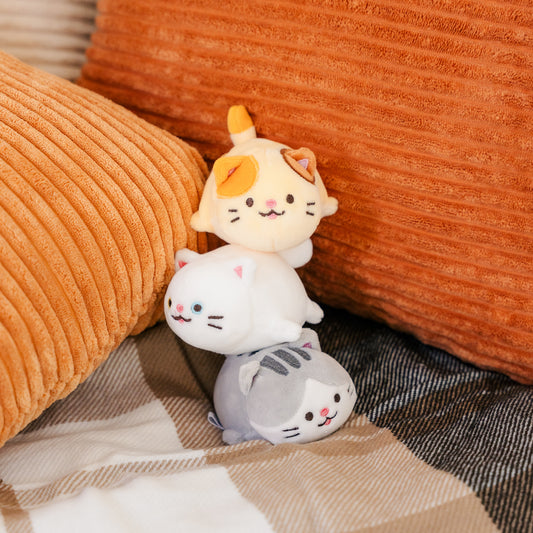 All three cat plushies stacked on top of each other against orange pillows.