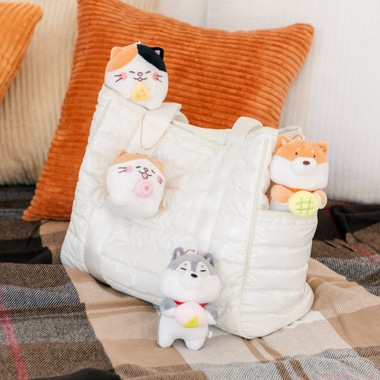 Four keyrings, two dogs and two cats, are arranged on and around a white bag. One cat is attached to the bag's handle and a dog peeks out of a bag pocket.
