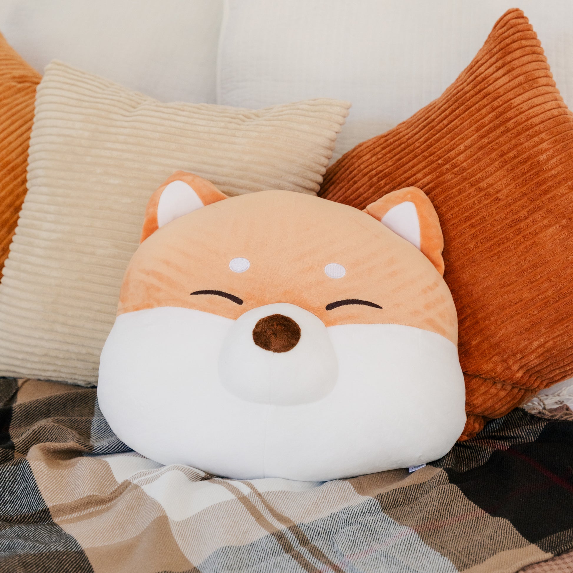 Shiba cushion nestled among blankets and pillows.