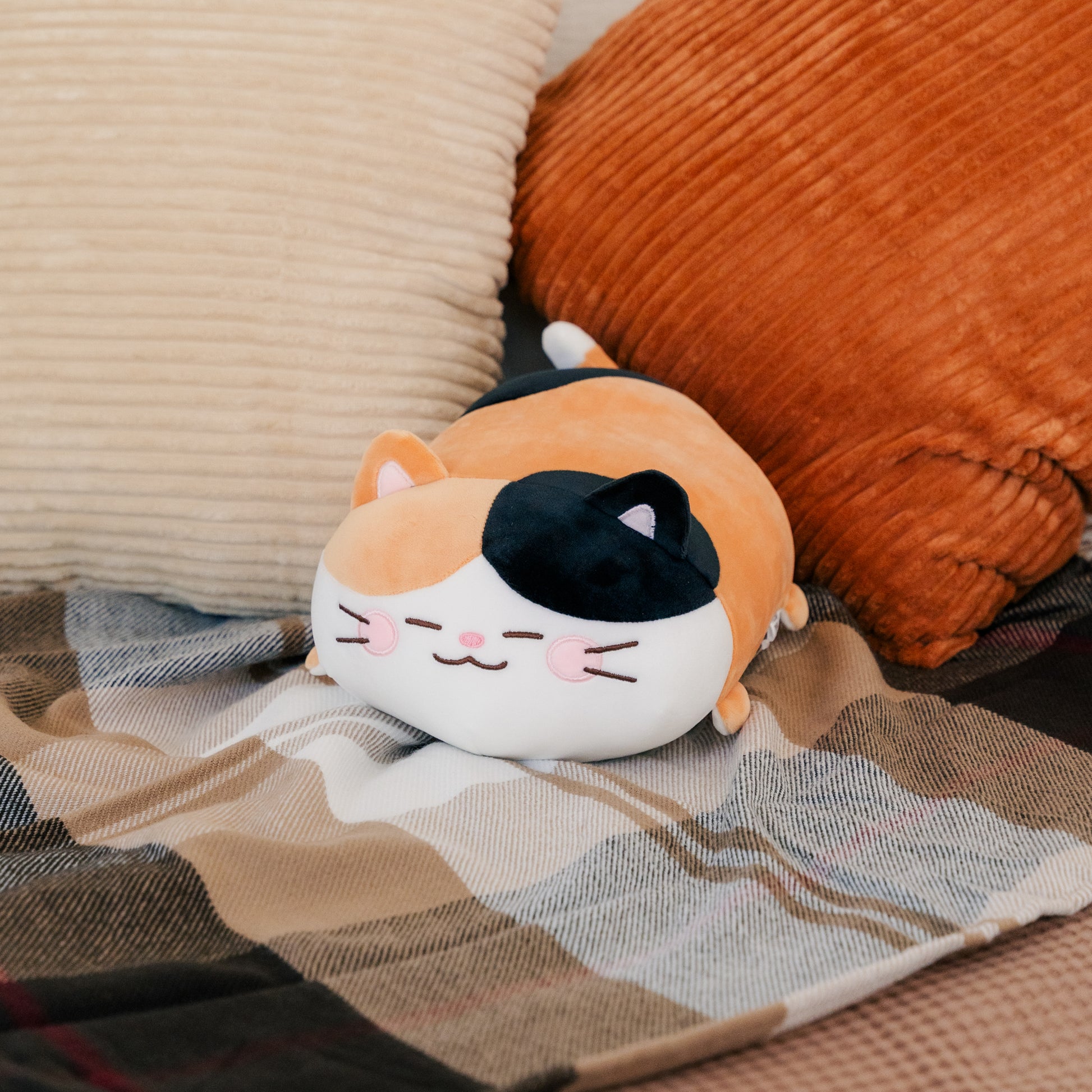 Camang plush resting peacefully on a blanket with pillows.