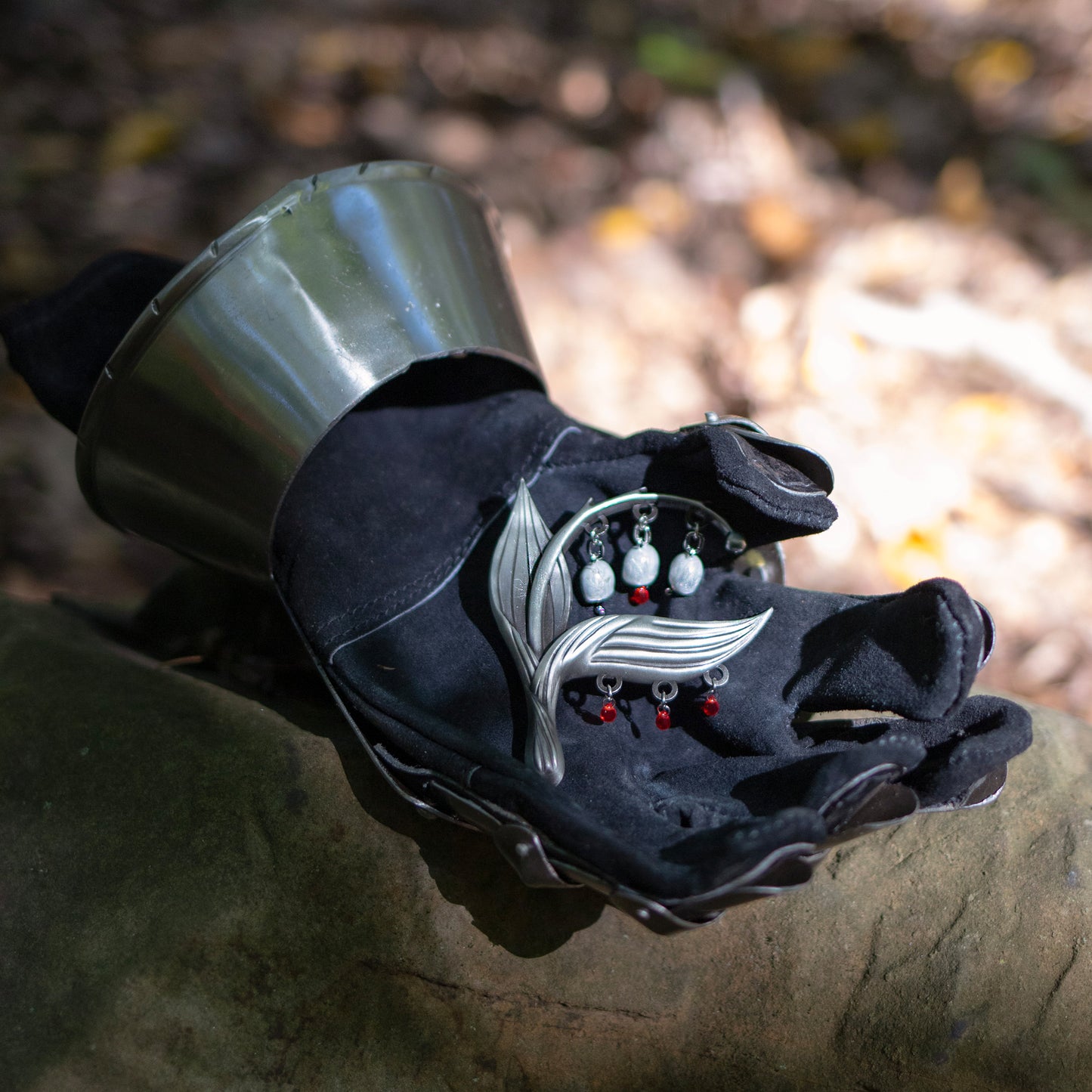 The Sacred Blood Pin is resting in the palm of a gloved medieval gauntlet in the forest.
