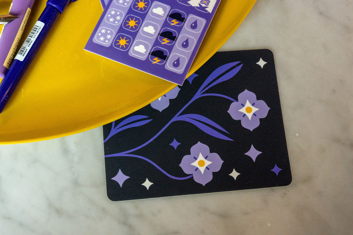The Speedwell Cover Sticker photographed next to a yellow tray with pens and stickers on a white marble background.
