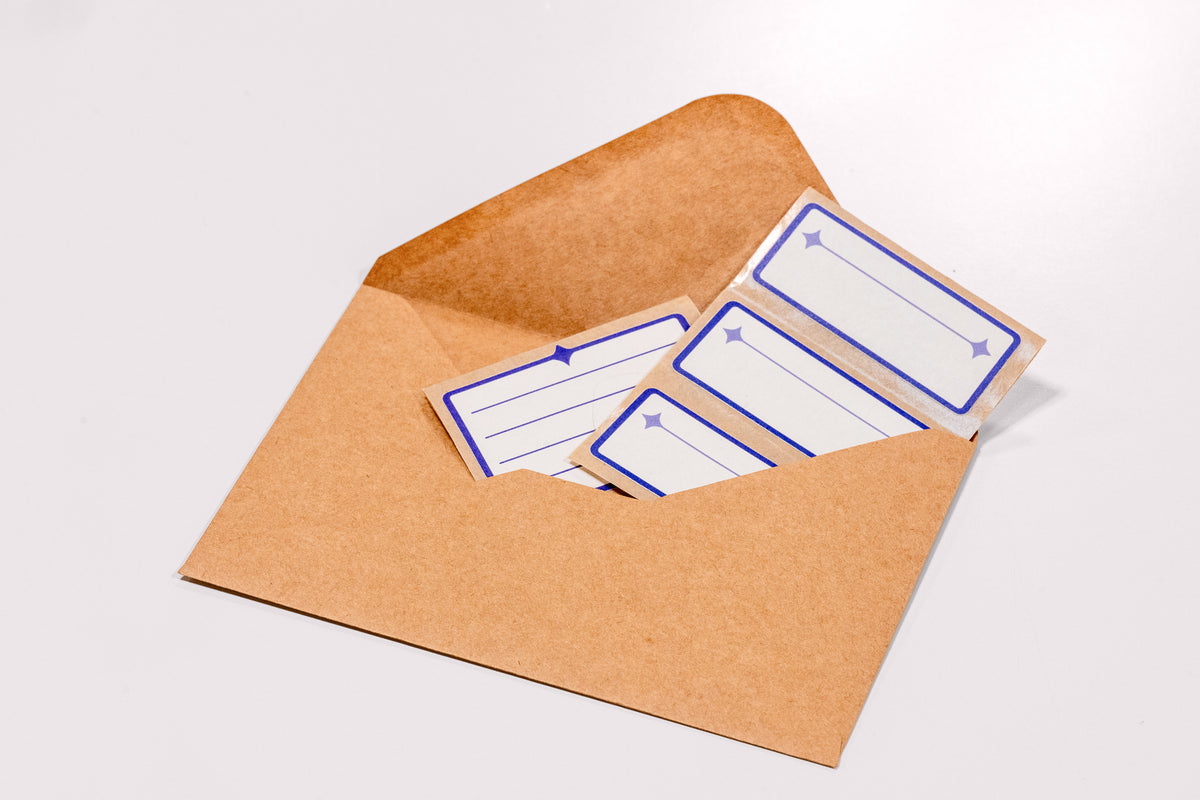 An array of white and indigo Nameplate Stickers peeking out of a brown kraft envelope on a white background.
