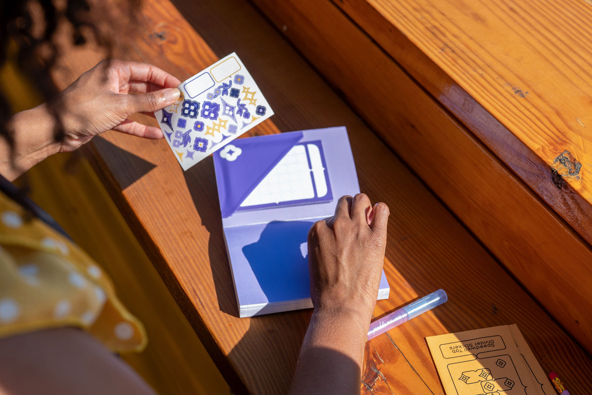 A person shows off the Speedwell Art Stickers against the Calendar Sticky Note nestled inside the pocket made from the Flower Pocket Sticker.