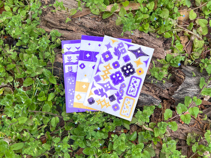 An array of a single sheet of the Speedwell Art Stickers, Icon Stickers, and Tab Divider Stickers photographed against the vibrant green and indigo of living speedwell flowers.