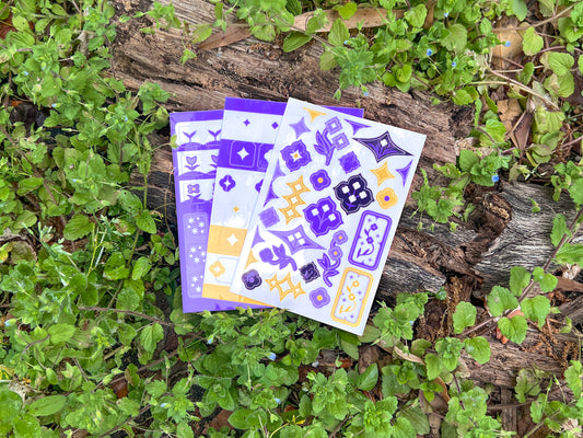An array of a single sheet of the Speedwell Art Stickers, Icon Stickers, and Tab Divider Stickers photographed against the vibrant green and indigo of living speedwell flowers.