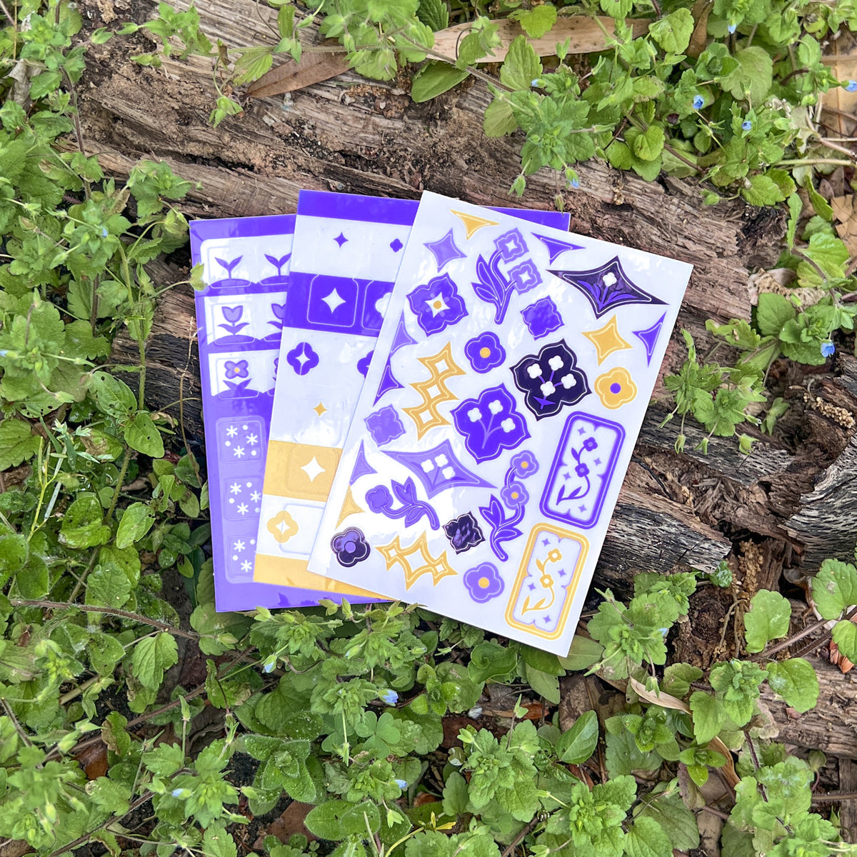 An array of a single sheet of the Speedwell Art Stickers, Icon Stickers, and Tab Divider Stickers photographed against the vibrant green and indigo of living speedwell flowers.