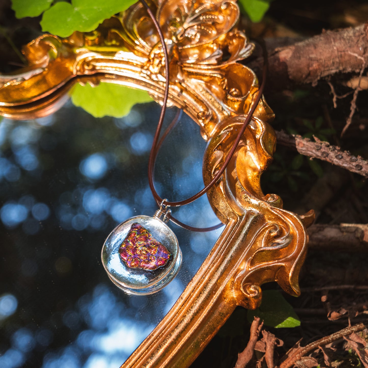 the ember glass pendant lying on a golden mirror, reflecting trees.