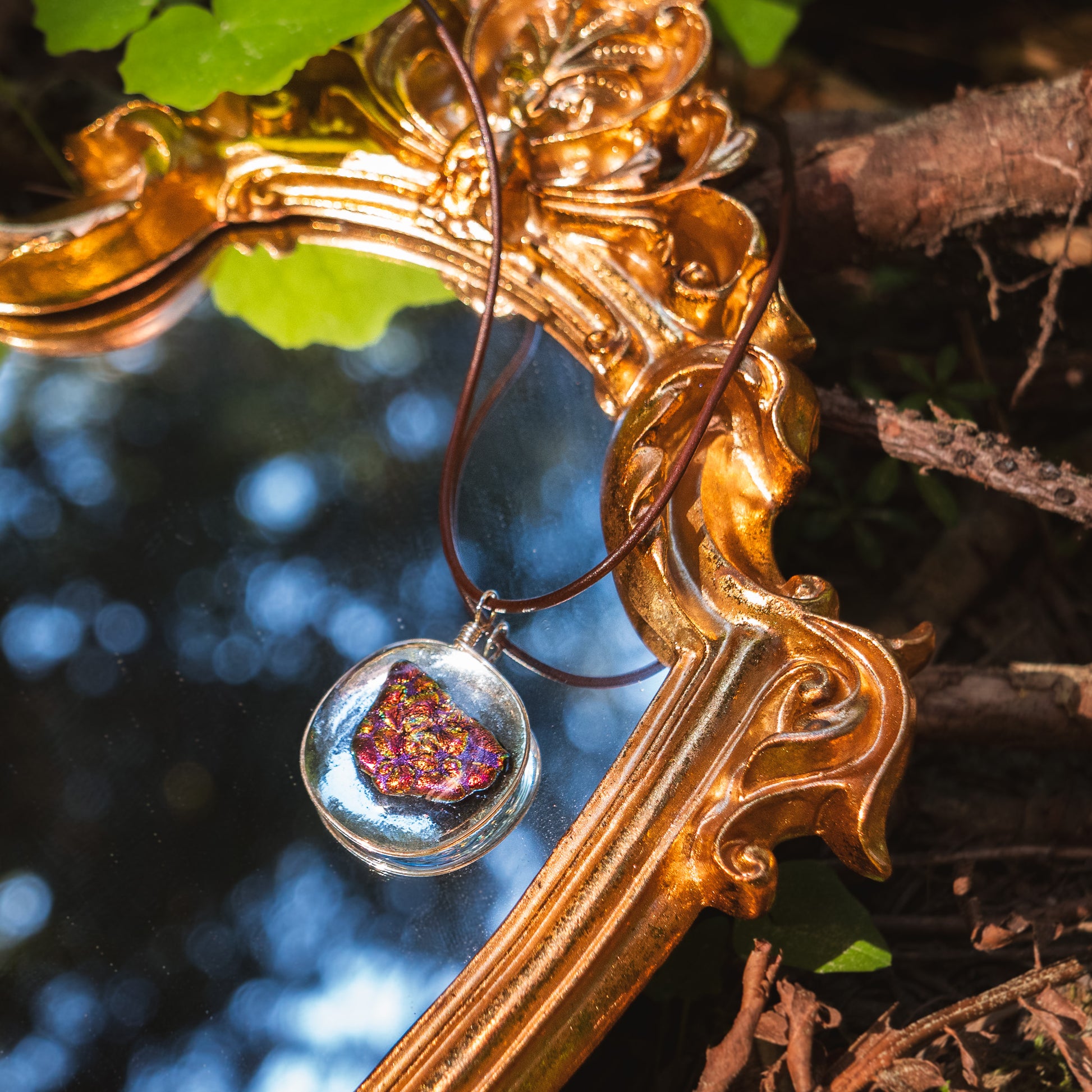 the ember glass pendant lying on a golden mirror, reflecting trees.