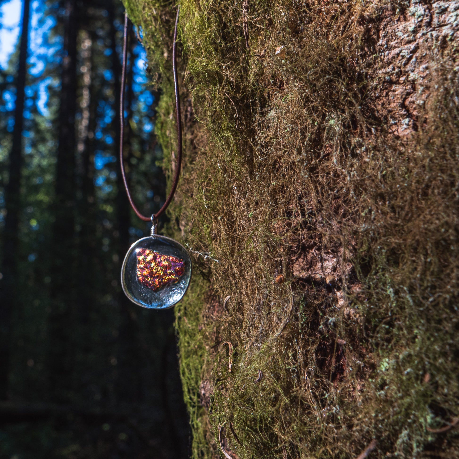 the ember glass pendant hanging next to a mossy tree trunk.