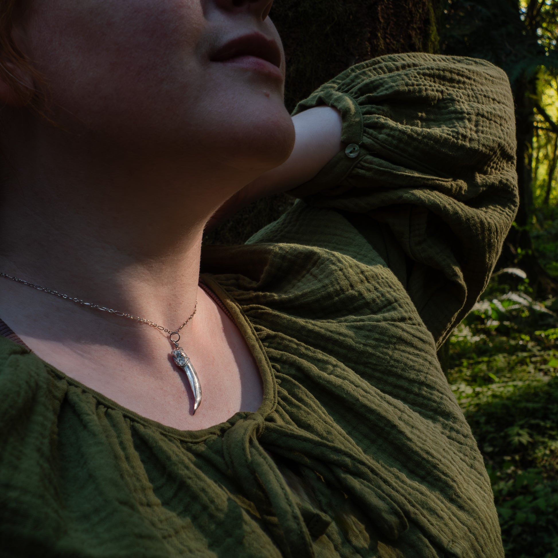 close-up photo of a model from the nose to mid-chest wearing the badger claw necklace and a rustic green shirt.