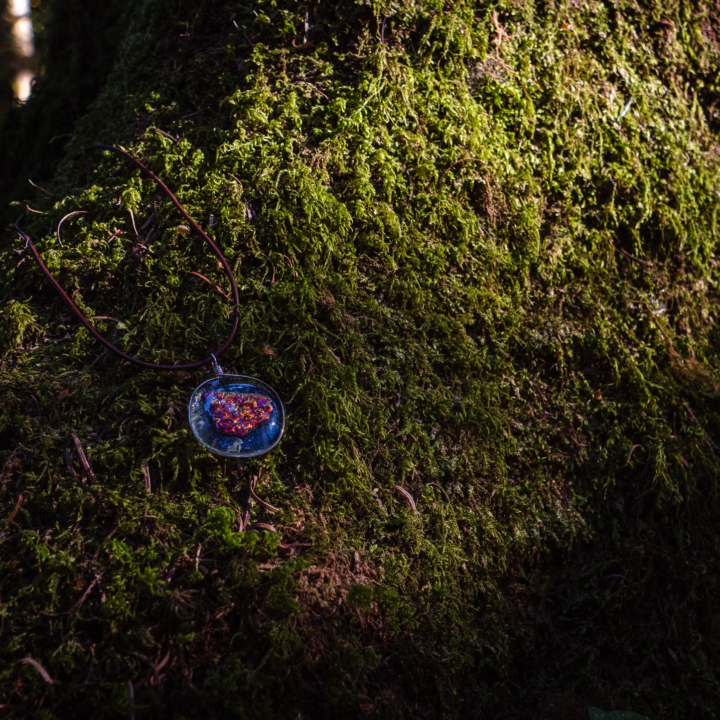 the ember glass pendant against a mossy background.
