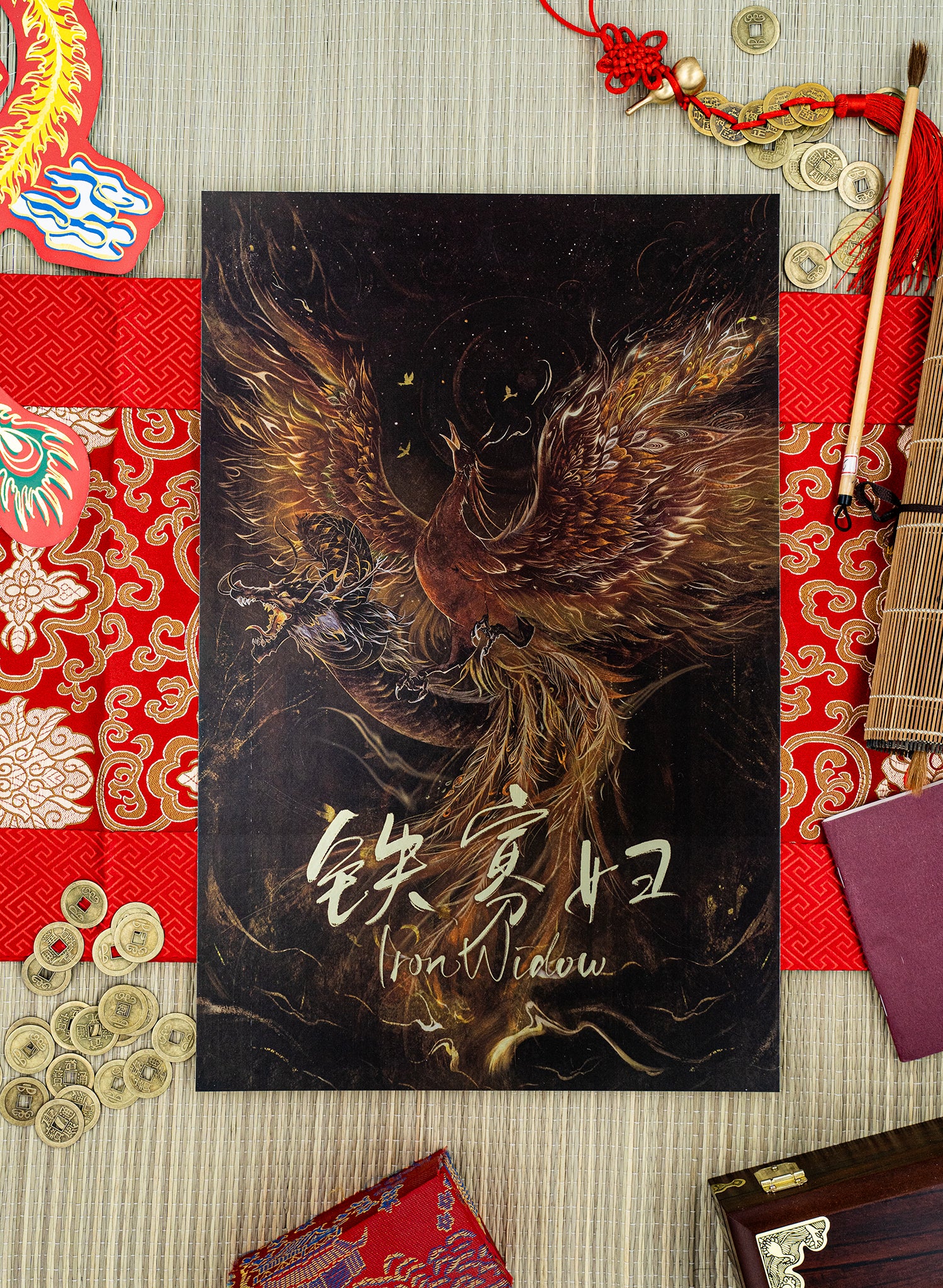Phoenix Over Dragon Print on a bamboo mat with red elaborate runner surrounded by decorations. 