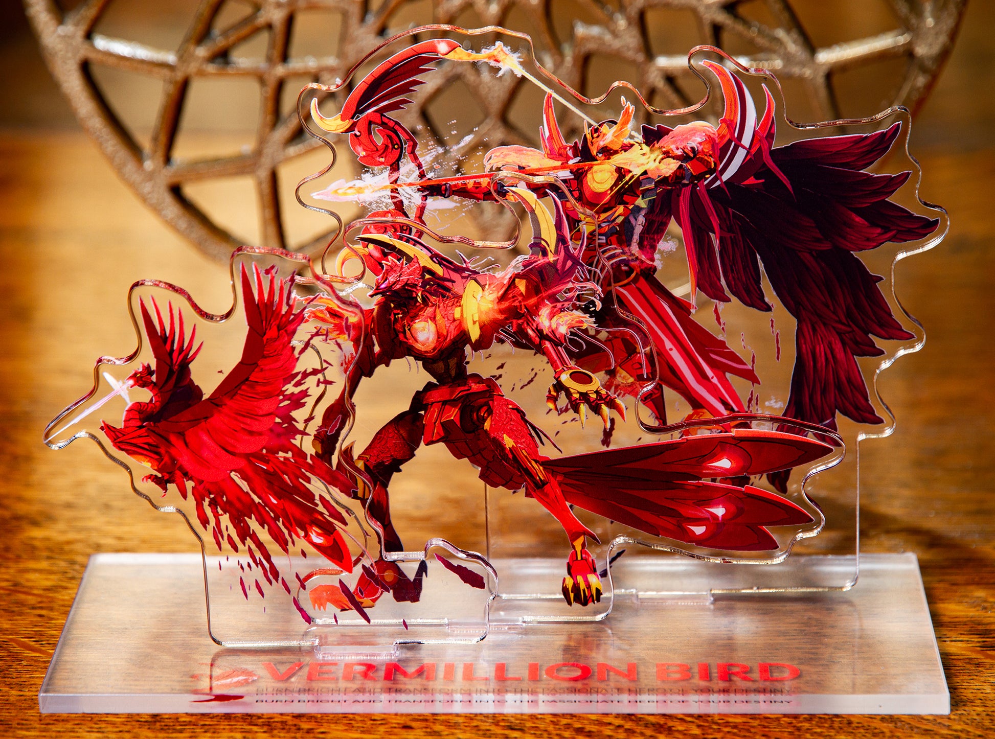 Vermillion Bird acrylic standee with warm wood and gold decoration in background.
