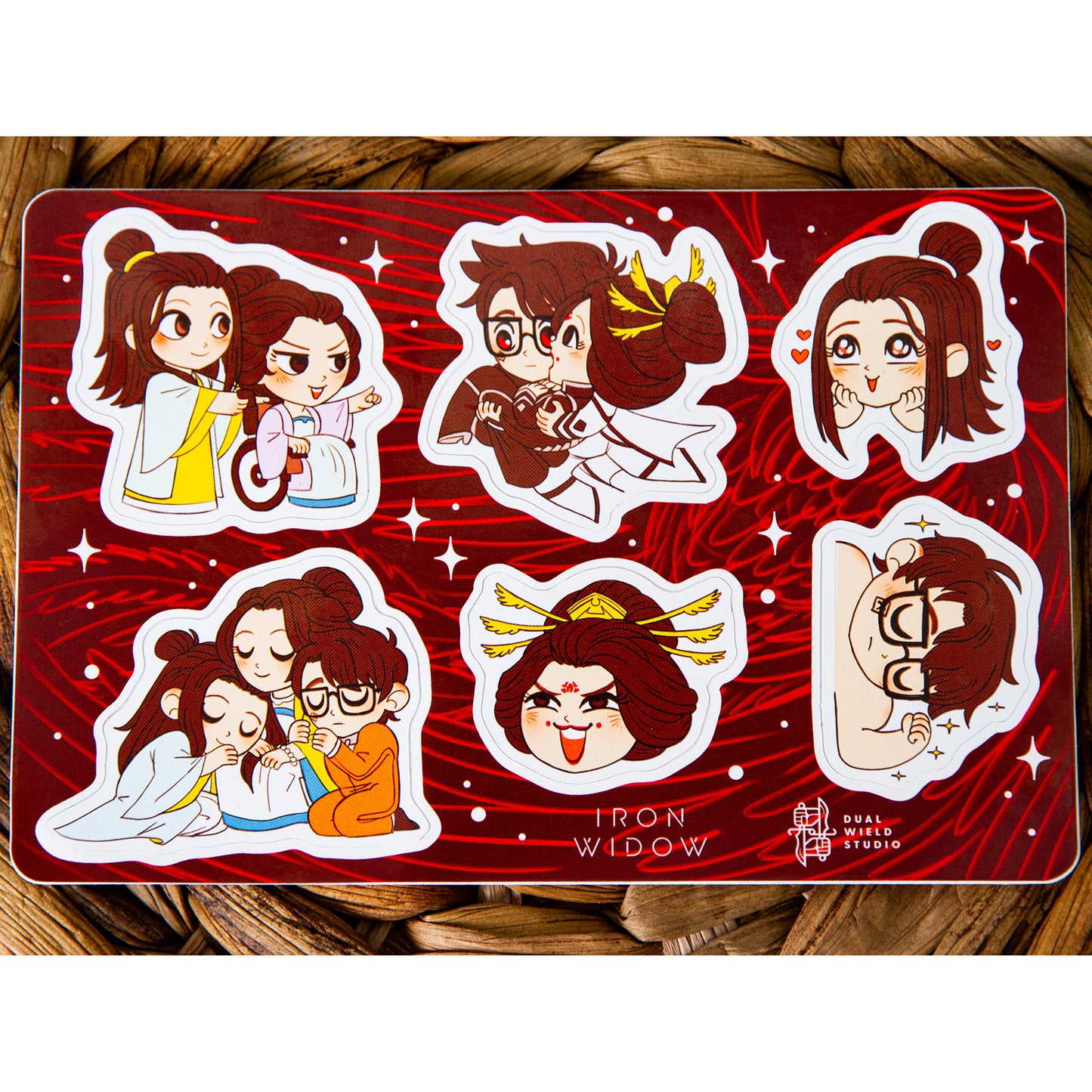 Iron Widow: Trio Sticker sheet resting on a warm brown wicker background.